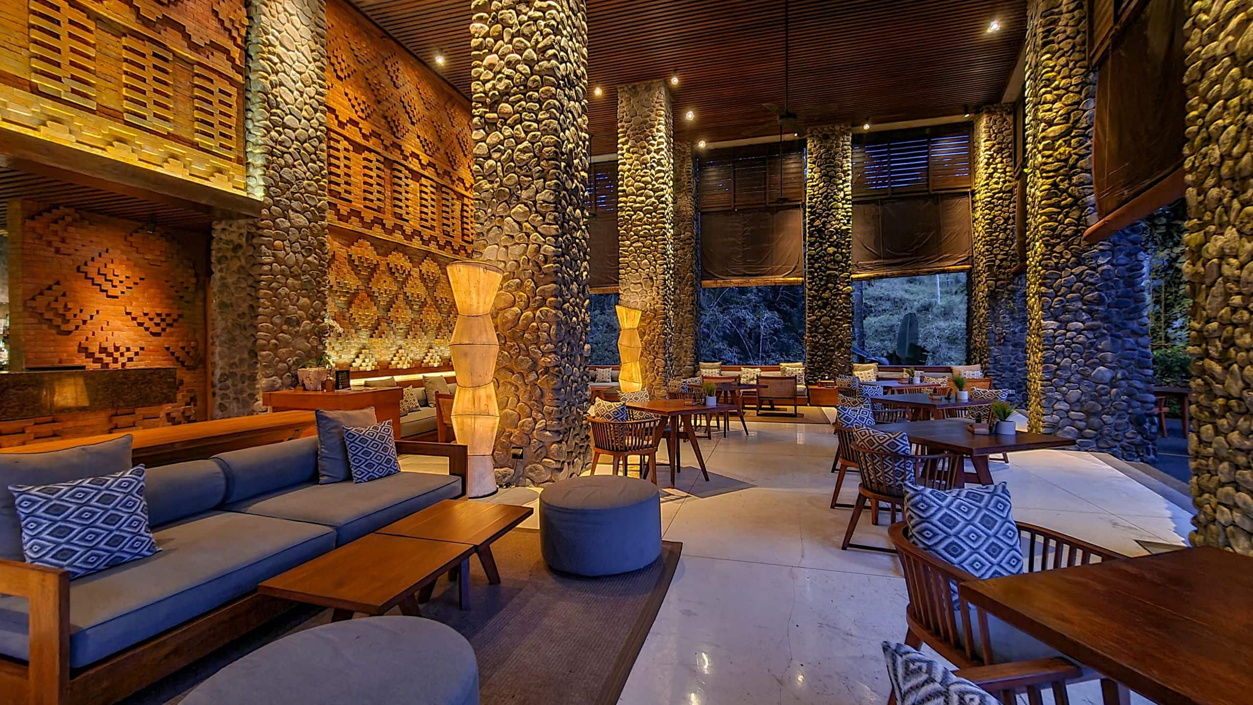 Terracotta walls, stone columns, sofas and tables lit by warm lamps at Cabana Lounge at night