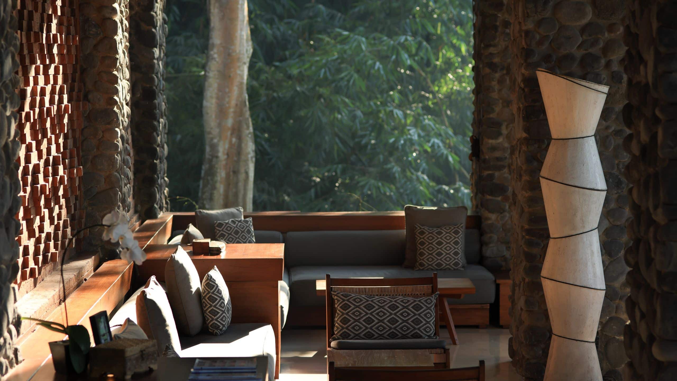 Cushioned wooden sofas beside terracotta walls and stone columns, facing the forest at Cabana Lounge