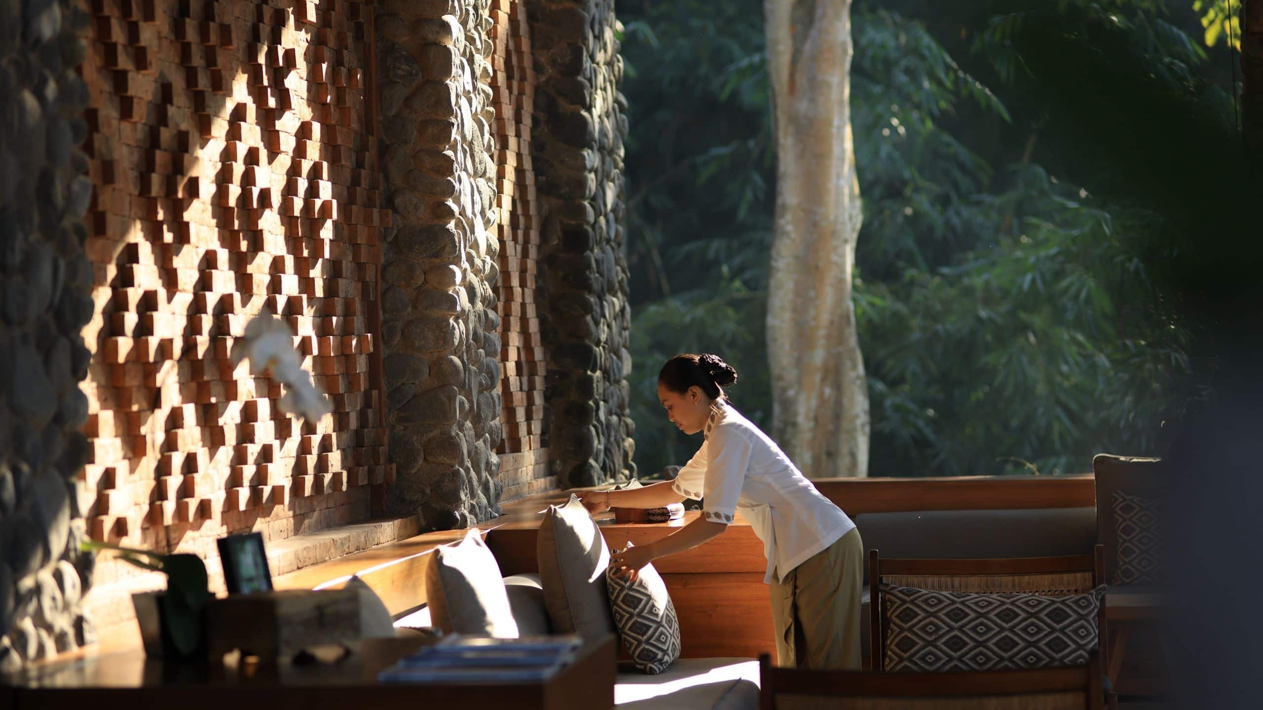 A Cabana Lounge team member arranges sofa cushions beside terracotta walls with forest beyond