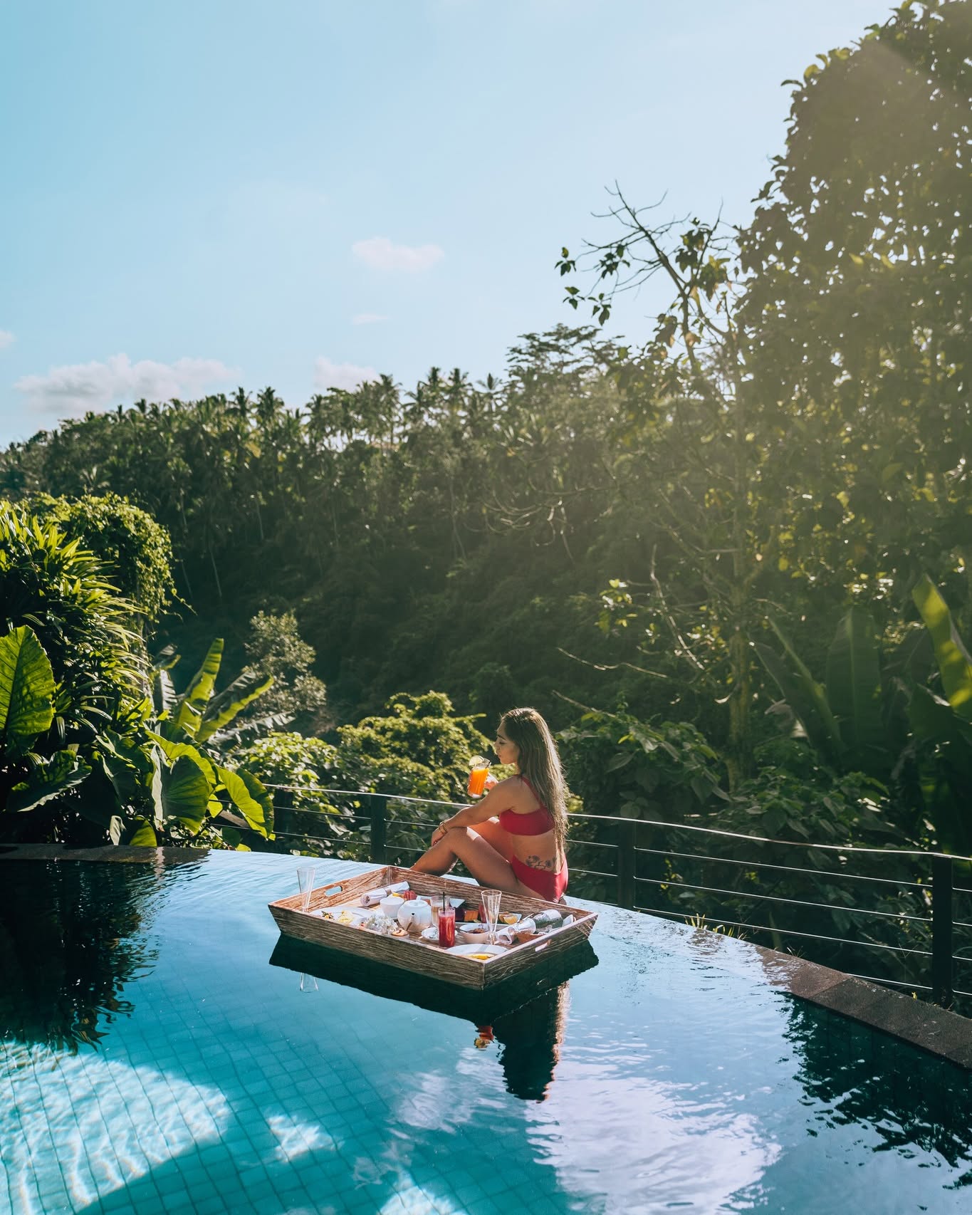 Seorang perempuan di samping nampan makanan terapung di kolam Awana yang menghadap hutan