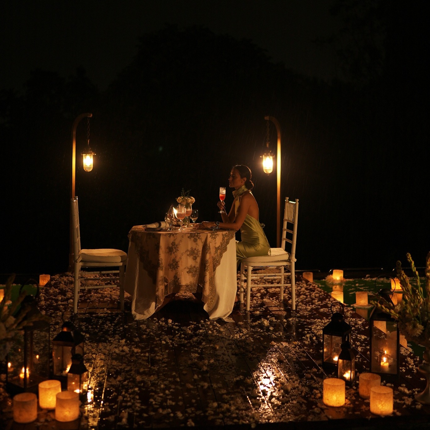 Seorang perempuan duduk di meja yang dikelilingi lilin dan lentera di atas Awana Pool pada malam hari