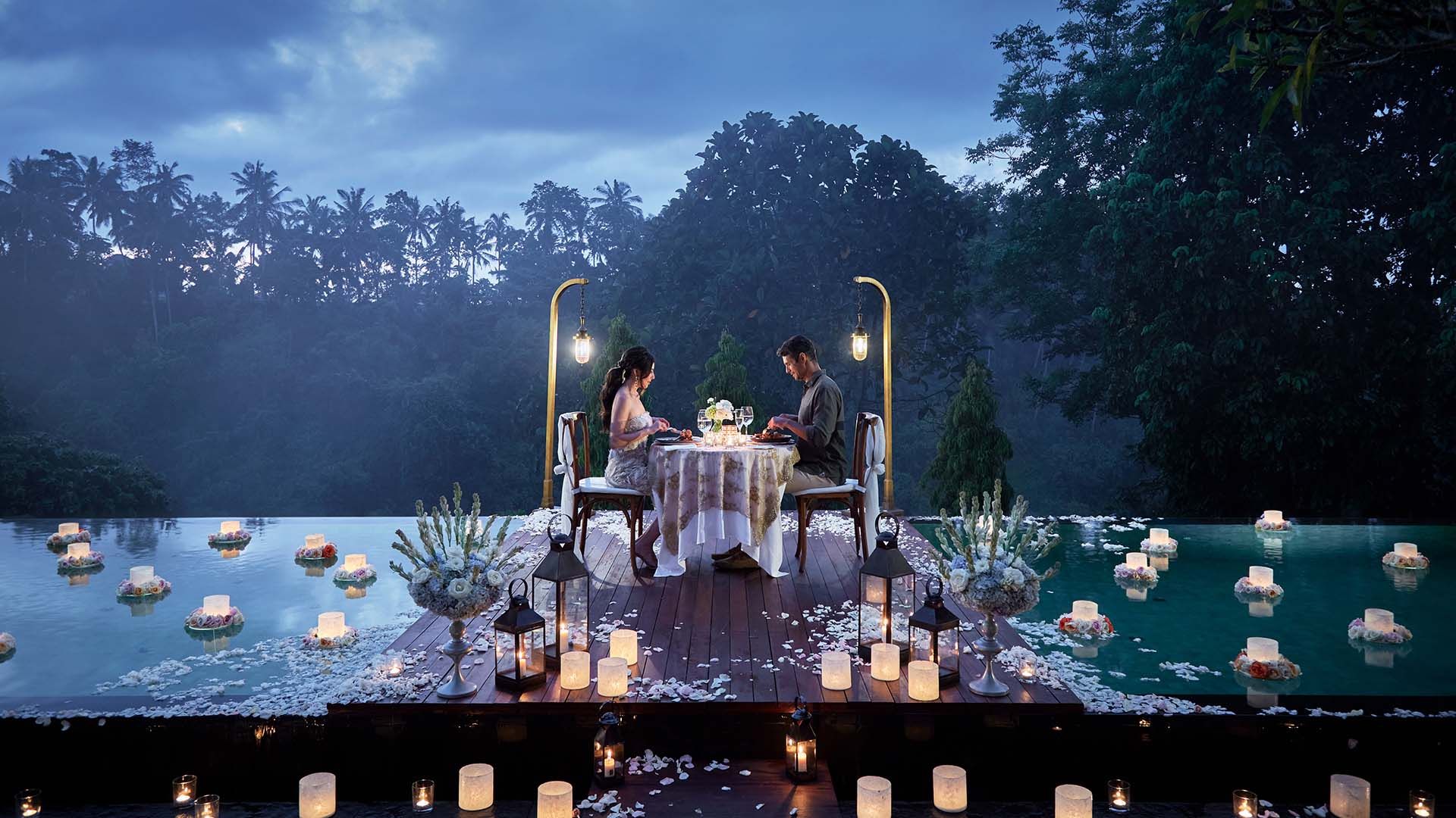 Pasangan bersantap malam di platform terapung dengan lilin di Awana Pool & Lounge