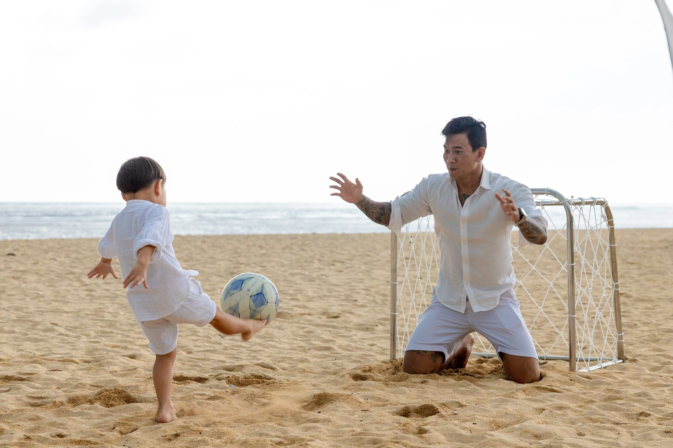 A parent and child playing football by the sea