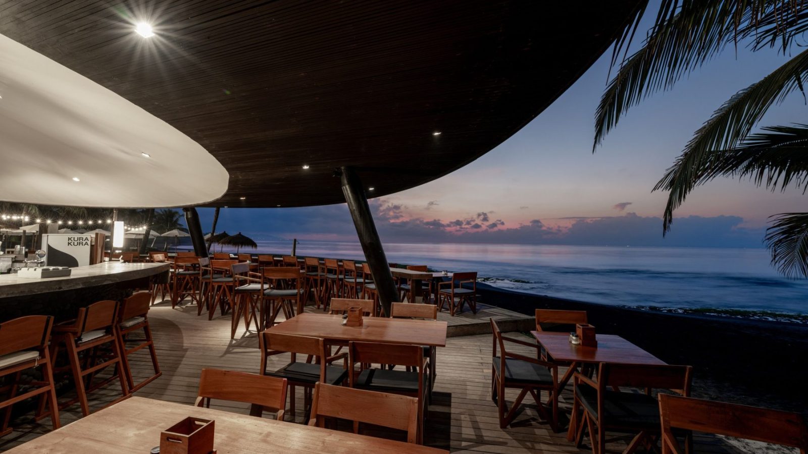 Deck restaurant tepi laut saat sore di Komune Beach Club Keramas