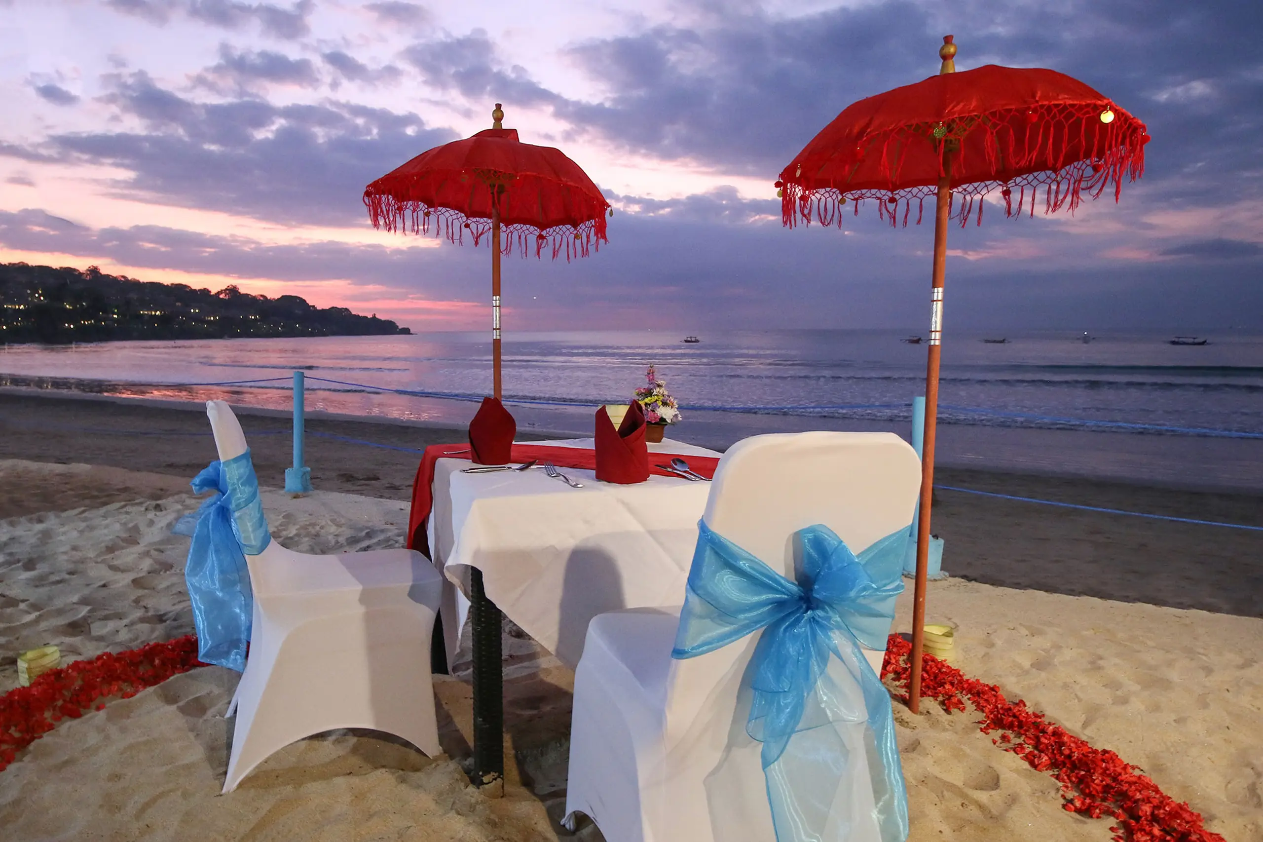 Kupu Kupu Jimbaran Beach Club — Meja pantai di bawah langit senja