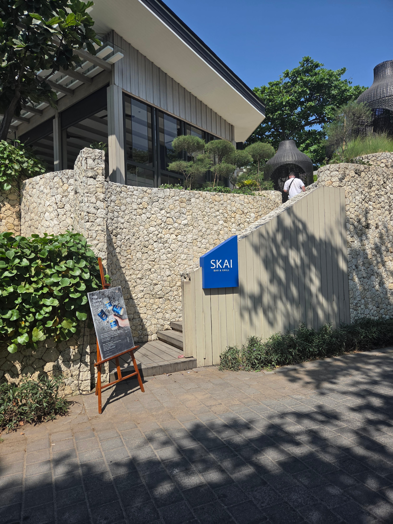 青いSKAI Bar & Grillの看板と石壁沿いの階段がある入口
