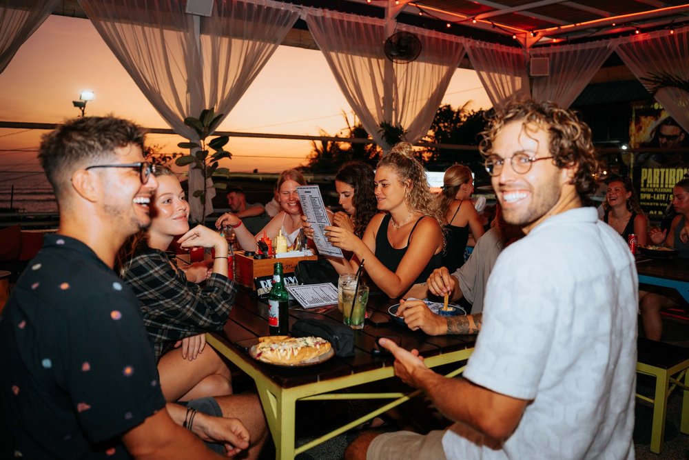 Guests enjoying pizza and drinks against a sunset sky